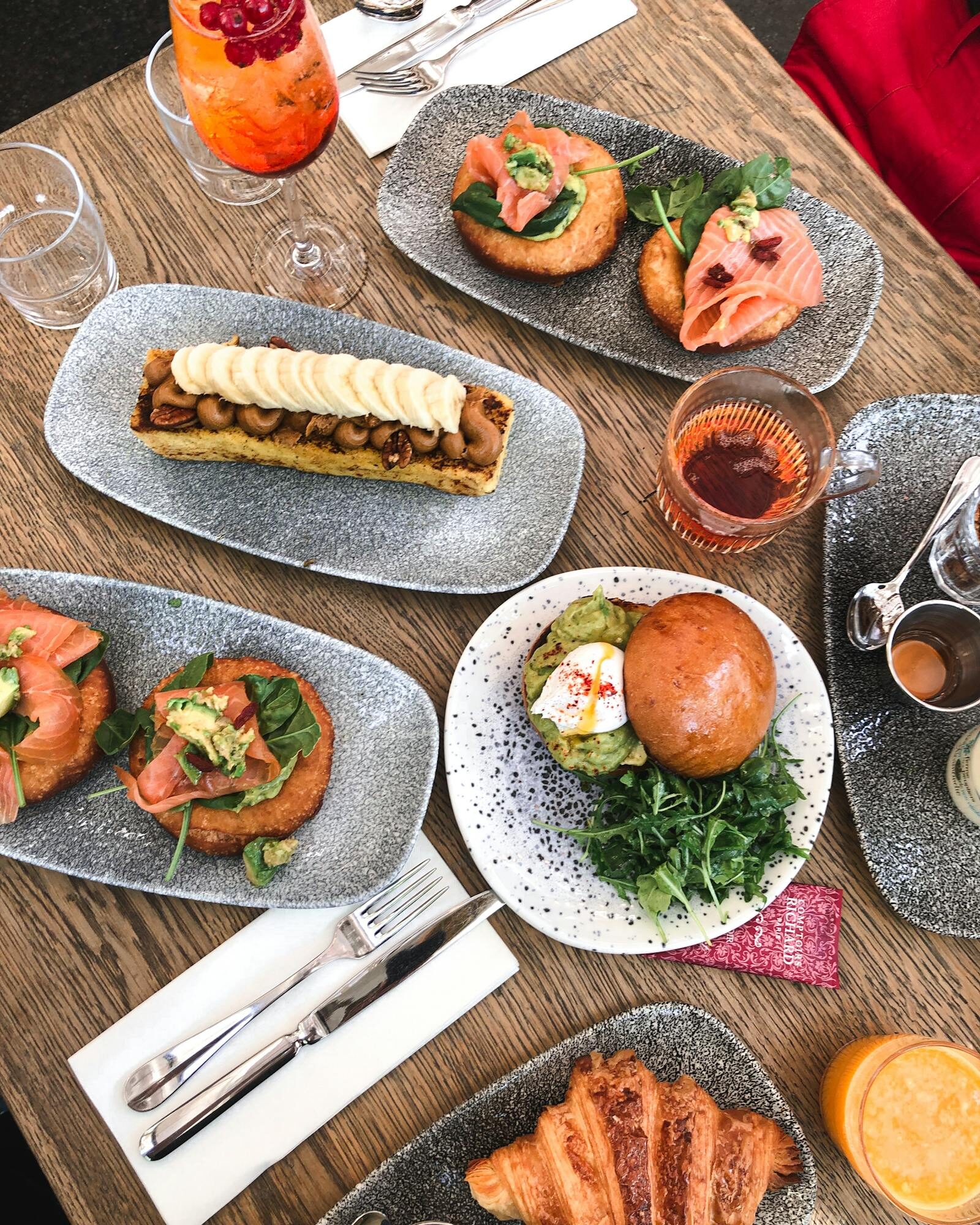 Top-down brunch spread with breakfast dishes and drinks, hands reaching across the table