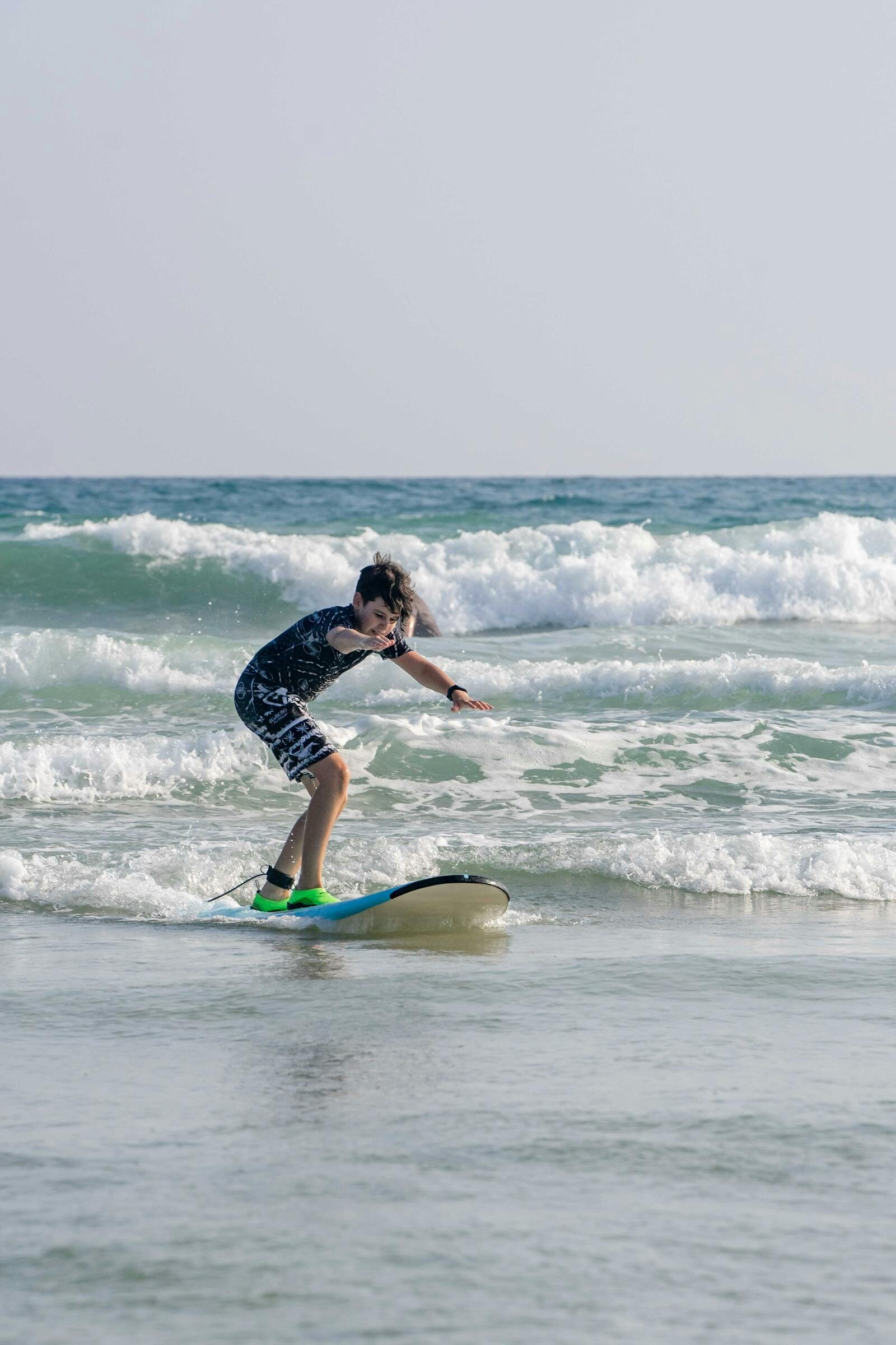 Beginner riding a whitewash wave on a soft-top, big smile, learning to surf in Taghazout, Morocco